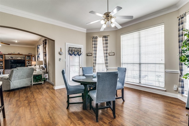 dining room featuring crown molding, arched walkways, dark wood finished floors, and a ceiling fan