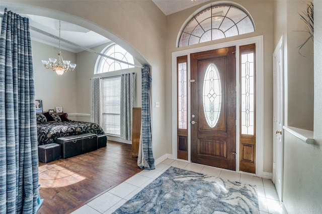 tiled entryway with baseboards, ornamental molding, arched walkways, and a notable chandelier