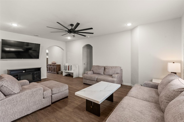 living area with arched walkways, dark wood-type flooring, a glass covered fireplace, and recessed lighting