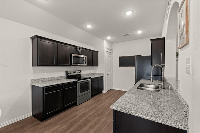 kitchen with light stone counters, a sink, baseboards, appliances with stainless steel finishes, and dark wood finished floors