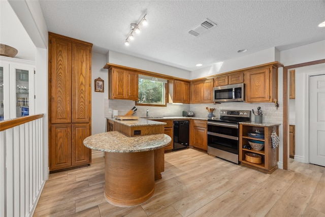 kitchen featuring stainless steel appliances, light wood-style flooring, brown cabinetry, and visible vents