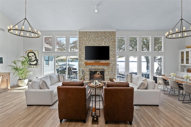 living area with a chandelier, visible vents, a towering ceiling, a brick fireplace, and light wood finished floors