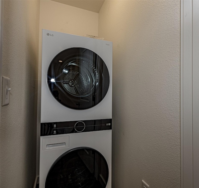 laundry area with a textured wall, laundry area, and stacked washing maching and dryer