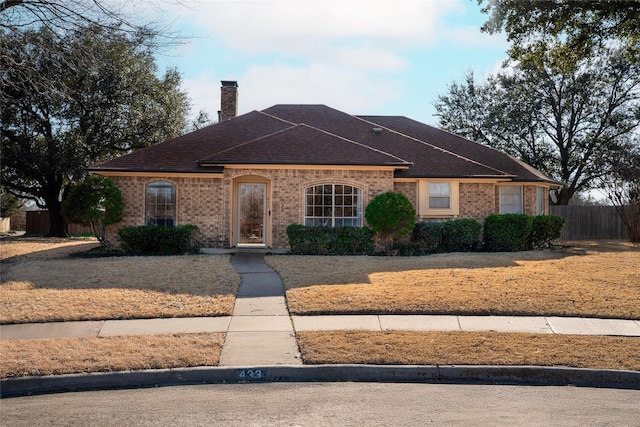 view of front of house with brick siding, a shingled roof, a chimney, and fence