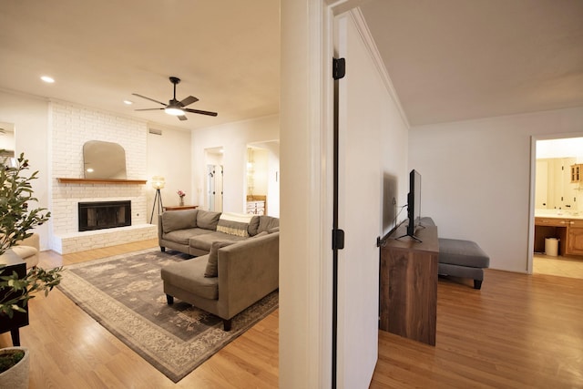 living area featuring light wood-style floors, crown molding, a ceiling fan, recessed lighting, and a brick fireplace