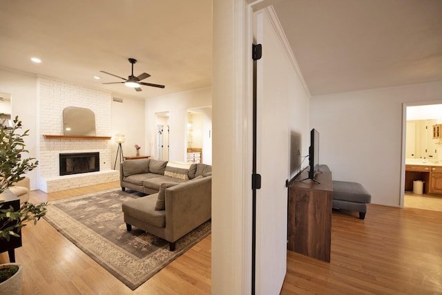 living area with a brick fireplace, crown molding, ceiling fan, recessed lighting, and light wood-style floors