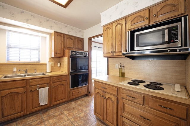 kitchen with stainless steel microwave, wallpapered walls, white electric stovetop, dobule oven black, and a sink