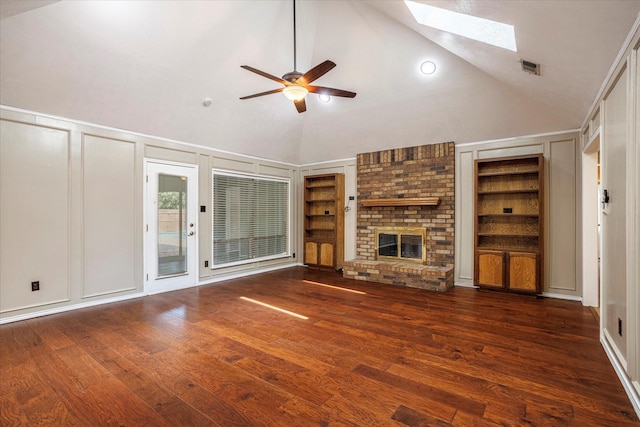 unfurnished living room featuring a skylight, dark wood finished floors, built in shelves, a decorative wall, and a fireplace