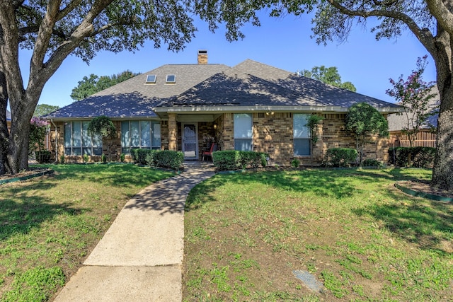 view of front of house featuring brick siding, a chimney, a front yard, and a shingled roof