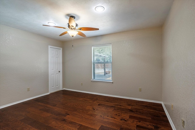 spare room featuring a textured wall, dark wood-type flooring, a ceiling fan, and baseboards