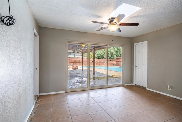 empty room with light tile patterned floors, baseboards, a ceiling fan, and a textured wall