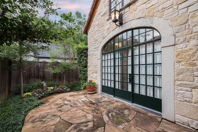 exterior entry at dusk featuring stone siding, a patio area, and fence