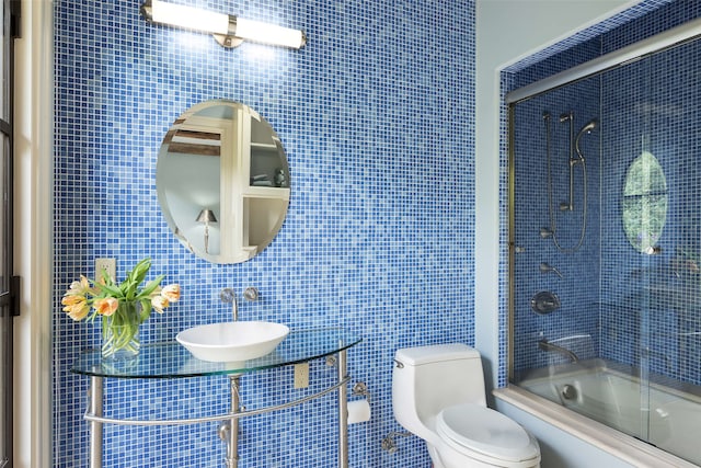 full bath with a sink, tile walls, toilet, and bath / shower combo with glass door