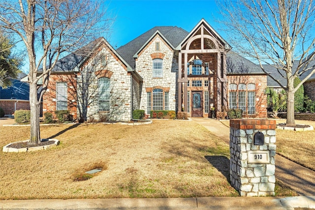 french provincial home with stone siding, brick siding, and a front lawn