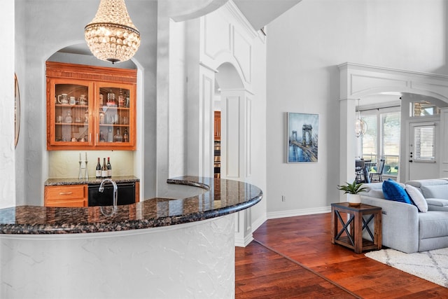 bar featuring a notable chandelier, a towering ceiling, baseboards, dark wood-style floors, and pendant lighting