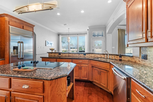 kitchen featuring brown cabinetry, a kitchen island, hanging light fixtures, stainless steel appliances, and a sink