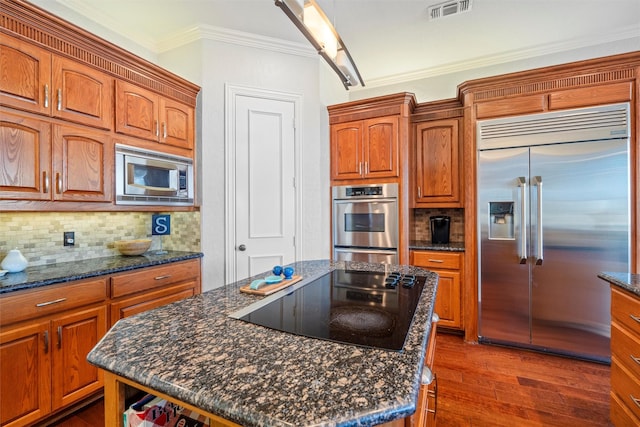 kitchen featuring built in appliances, a kitchen island, visible vents, and crown molding