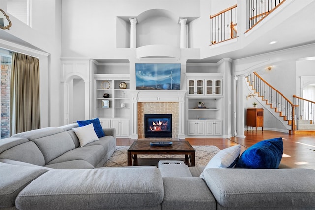 living room featuring a tile fireplace, a high ceiling, built in features, stairs, and light wood-style floors