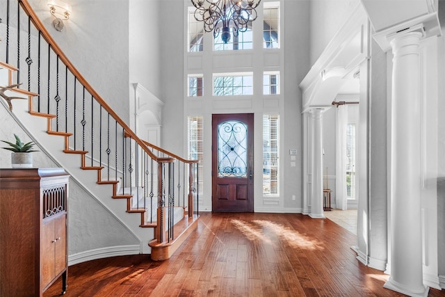 entrance foyer with wood-type flooring, stairway, a towering ceiling, an inviting chandelier, and ornate columns