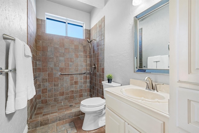 full bathroom with toilet, a textured wall, tiled shower, and vanity