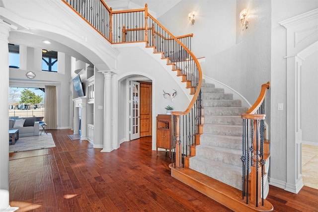 foyer with arched walkways, wood-type flooring, a towering ceiling, and ornate columns