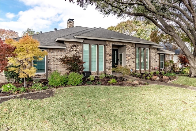 view of front of property featuring roof with shingles, brick siding, a chimney, and a front yard