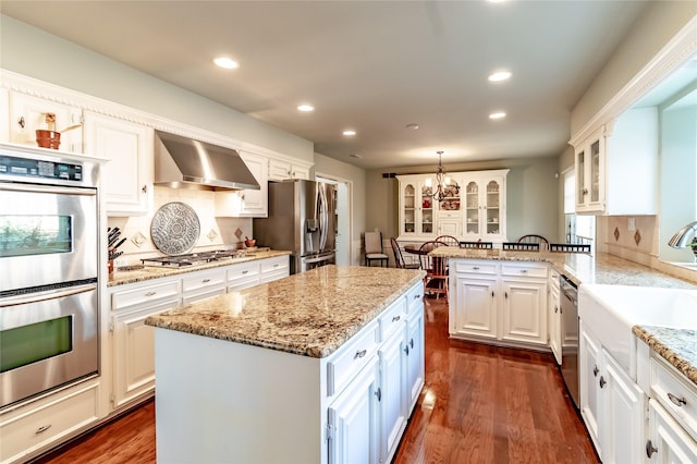 kitchen featuring stainless steel appliances, a kitchen island, white cabinetry, wall chimney exhaust hood, and pendant lighting