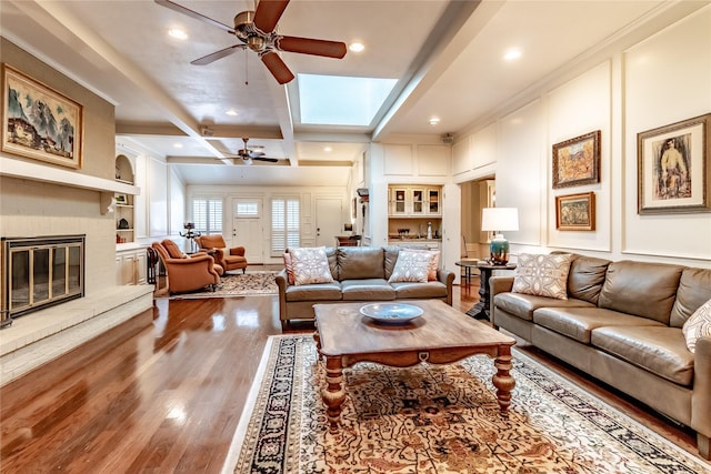 living room featuring a glass covered fireplace, wood finished floors, a ceiling fan, and a decorative wall