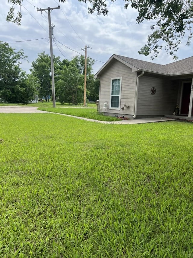 view of side of home featuring a yard and a shingled roof