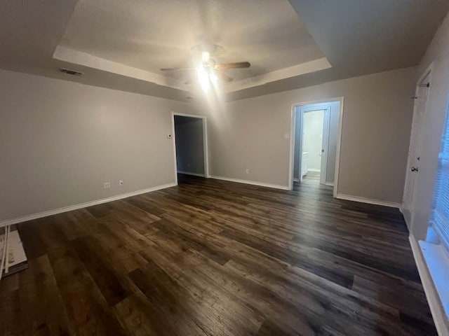 spare room with dark wood-style floors, baseboards, a tray ceiling, and a ceiling fan