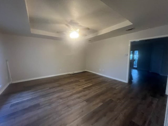 spare room featuring baseboards, visible vents, a raised ceiling, and dark wood finished floors