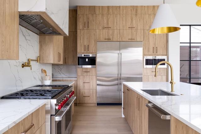 kitchen featuring high end appliances, modern cabinets, hanging light fixtures, custom exhaust hood, and a sink