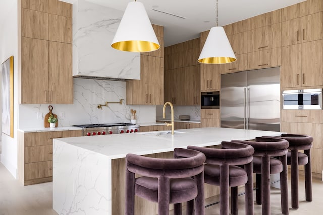 kitchen featuring an island with sink, modern cabinets, built in refrigerator, pendant lighting, and a sink