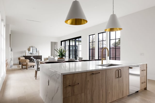 kitchen with hanging light fixtures, light wood-style floors, a kitchen island with sink, a sink, and modern cabinets