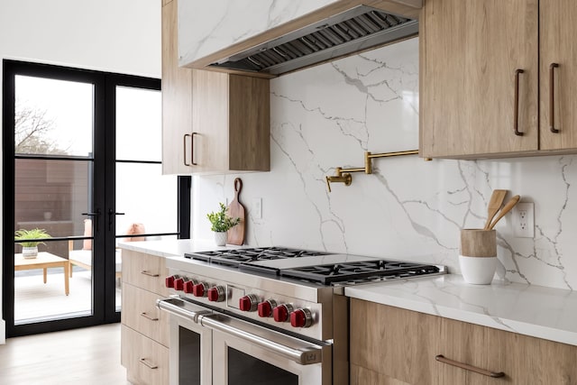 kitchen with tasteful backsplash, range with two ovens, custom range hood, modern cabinets, and light stone countertops