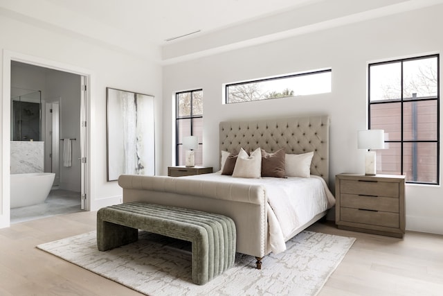 bedroom with light wood-style floors, multiple windows, and connected bathroom
