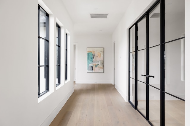 hallway with a wealth of natural light, light wood-type flooring, visible vents, and baseboards