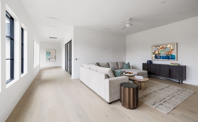 living room featuring light wood-style floors, visible vents, baseboards, and a ceiling fan