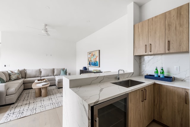 kitchen with wine cooler, a peninsula, a sink, open floor plan, and light stone countertops