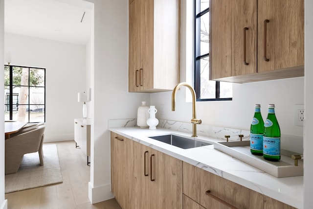 kitchen featuring light stone counters, a wealth of natural light, a sink, and light wood finished floors