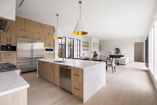 kitchen featuring built in fridge, a sink, hanging light fixtures, modern cabinets, and a center island with sink