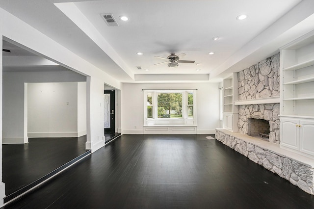 unfurnished living room featuring ceiling fan, a stone fireplace, visible vents, wood finished floors, and baseboards