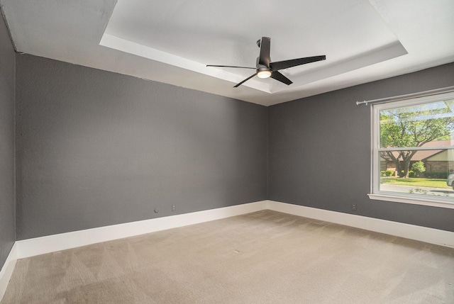 empty room with a raised ceiling, light carpet, and a ceiling fan