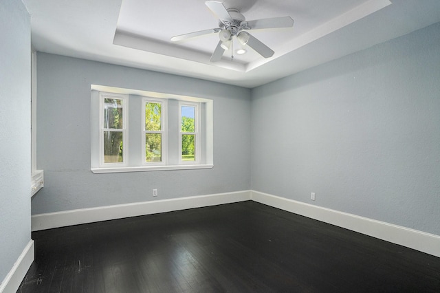spare room with dark wood-style flooring, baseboards, a ceiling fan, and a raised ceiling