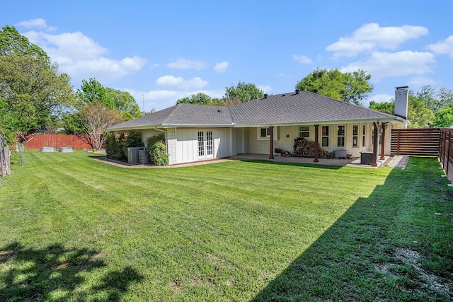 rear view of house with a yard, french doors, a fenced backyard, and a chimney