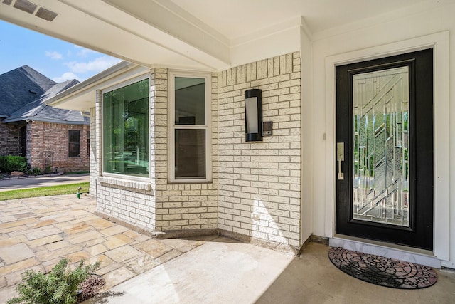 view of exterior entry featuring a patio area, brick siding, and visible vents