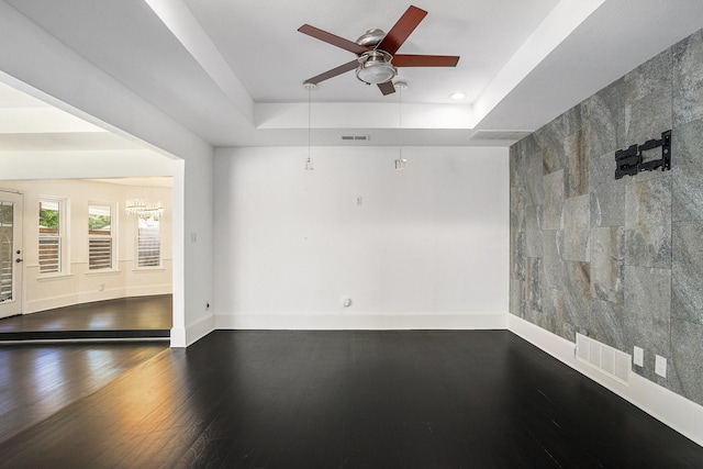 empty room with a tray ceiling, baseboards, a ceiling fan, and visible vents