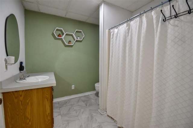 bathroom featuring toilet, vanity, a paneled ceiling, and baseboards