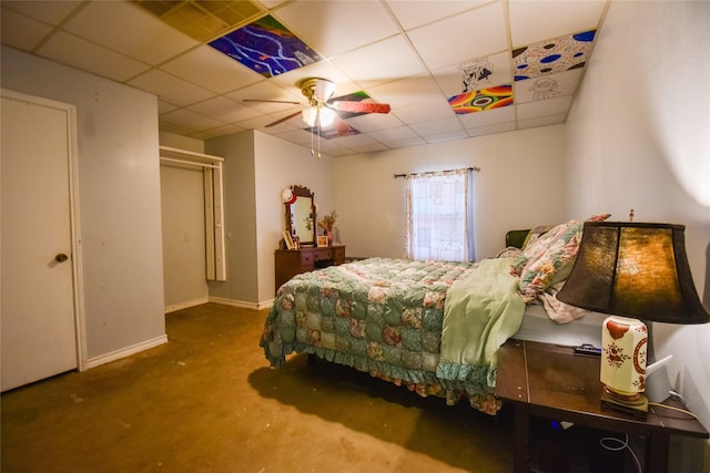 bedroom with a paneled ceiling, concrete floors, baseboards, and ceiling fan