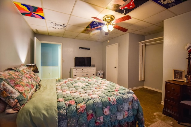 bedroom featuring concrete floors, a drop ceiling, a ceiling fan, and baseboards